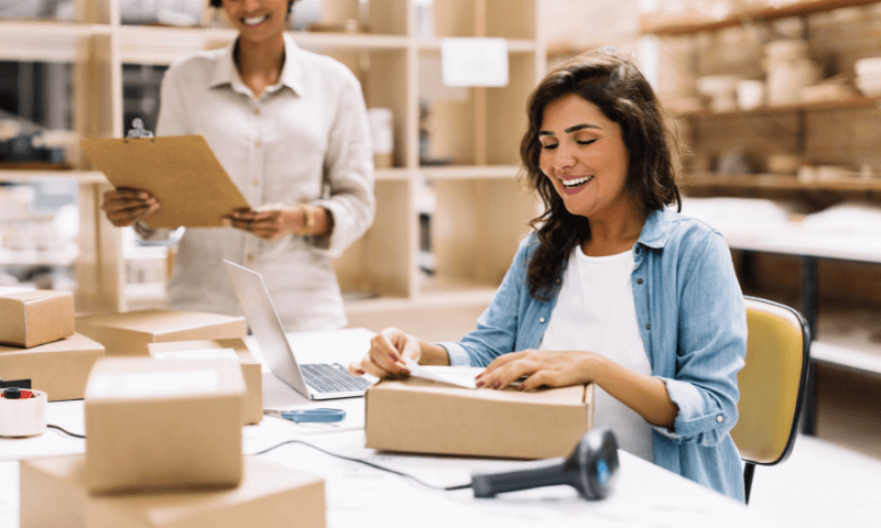 An excited woman putting a shipping label on top of a package after receiving a customer order from her business